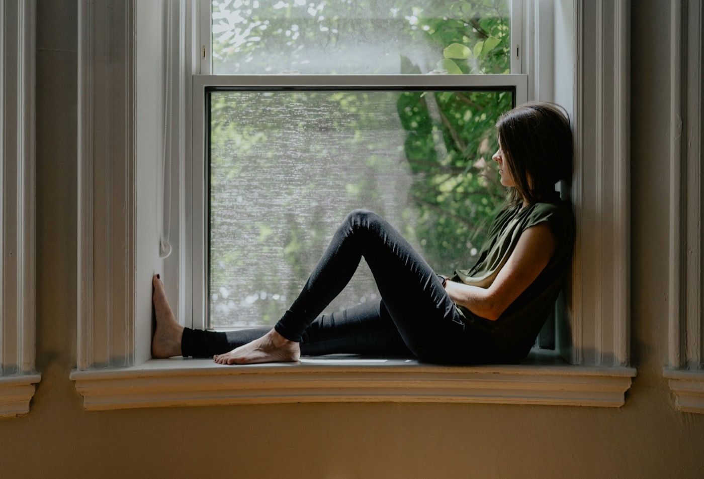 Woman sitting quietly on a window sill in soft daylight
